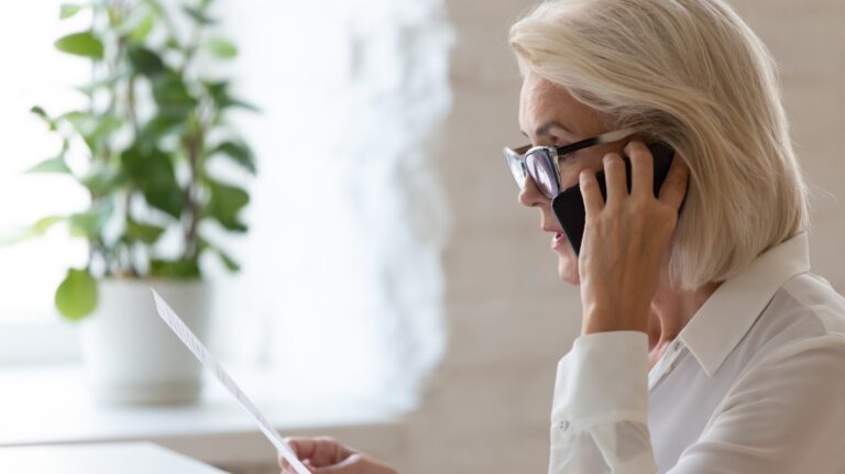 Serious senior woman talking on smartphone and reading document