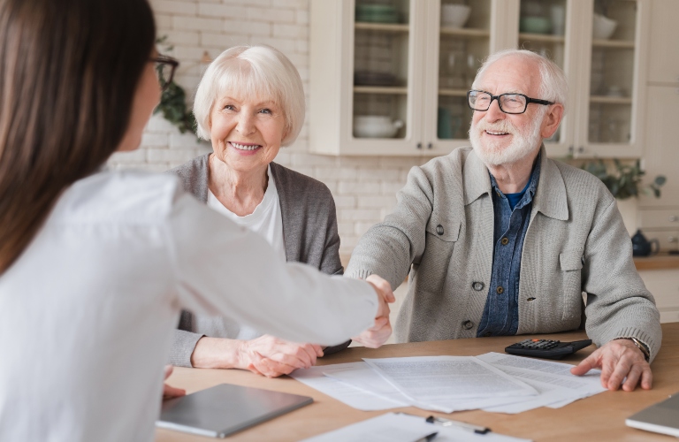happy senior couple shaking hands with lawyer