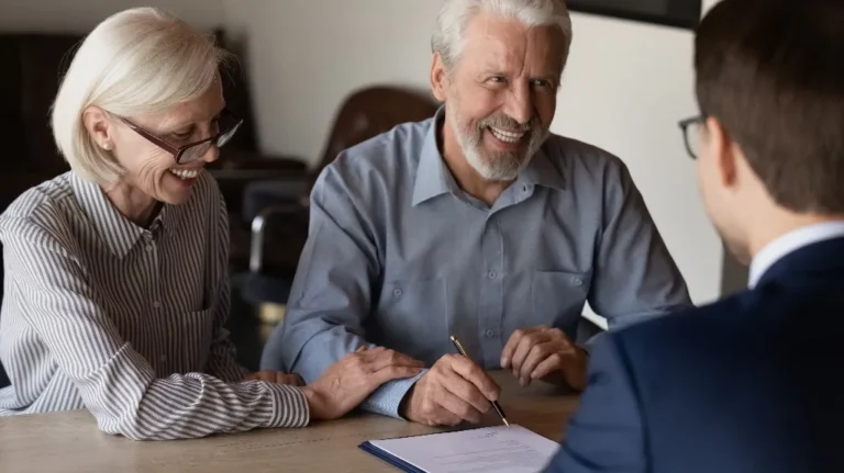 Elderly couple smiling and signing a document during a meeting with a professional.