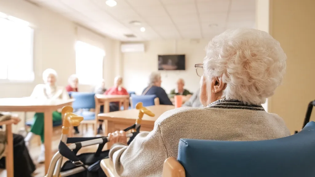 Elderly individuals seated in a well-lit room, engaged in group activity or discussion.