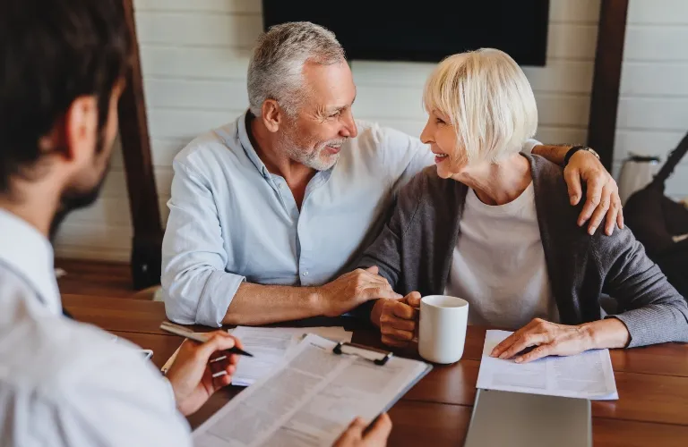 Mature couple smiling and holding hands during a meeting with a professional at a wooden table.