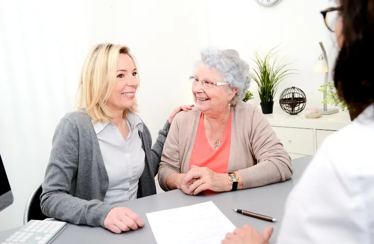 Elderly woman and middle-aged woman smiling during consultation with healthcare professional.